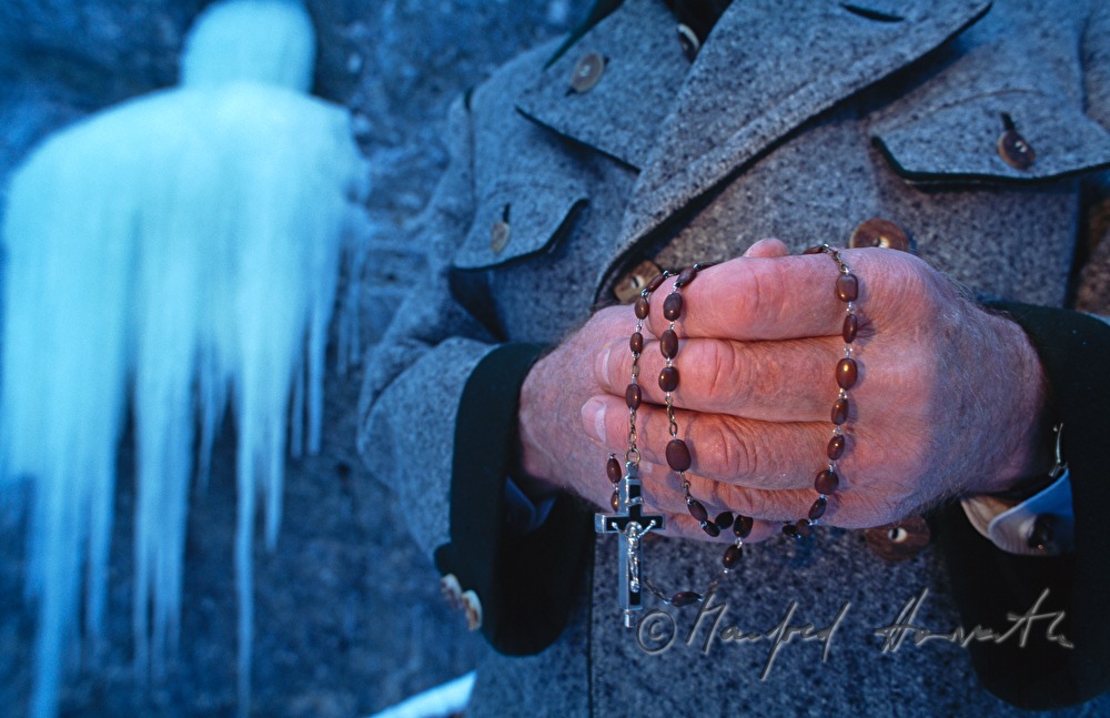 Wallfahrer mit Rosenkranz betet bei Wasserfall