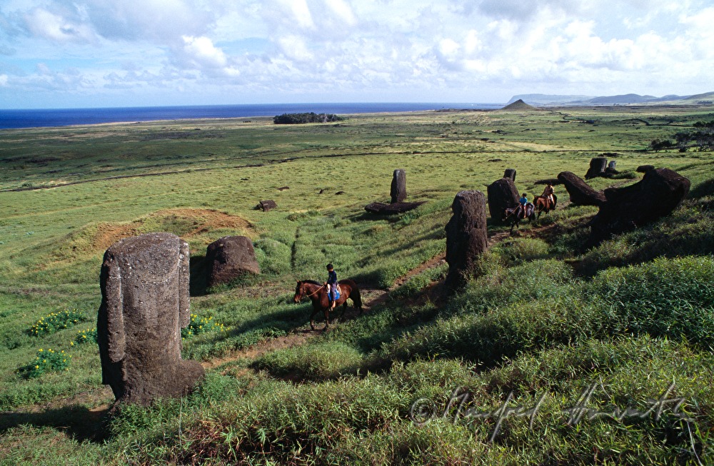 Reiter passieren Moai-Statuen am Fußm des Vulkans