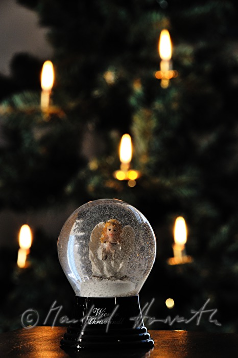 Schneekugel (mit Christkind) vor einem Weihnachtsbaum