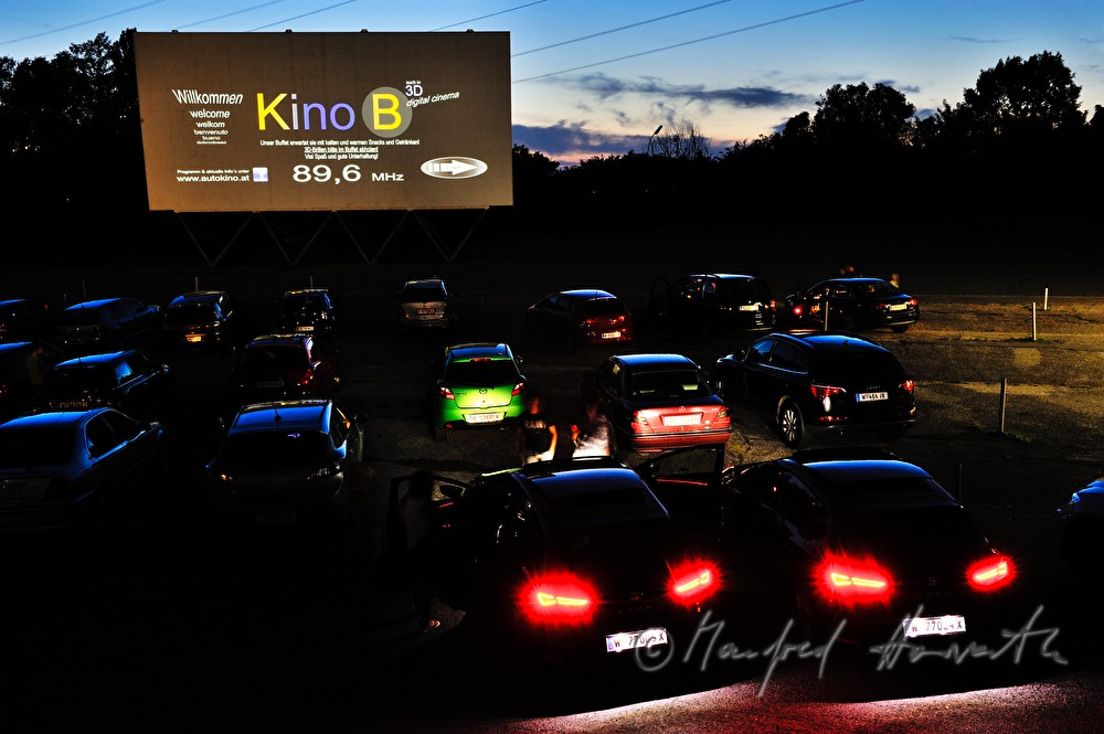 Autos vor der Kinoleinwand und  Anzeige für Autoradio-Frequenz