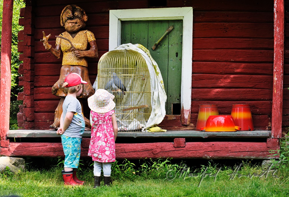 Kinder vor einem Bauernhaus mit Vogelkäfig