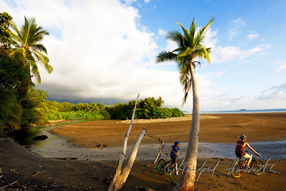 Mountainbiker durchqueren einen Flußlauf am Meeresstrand