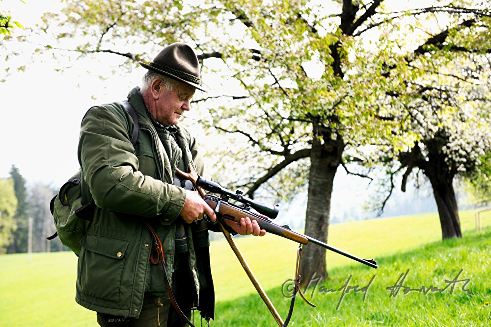 Jäger entsichert sein Gewehr in einer Obstplantage