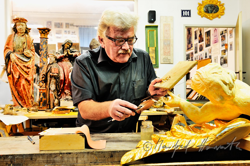 Vergolder trägt mit dem Anschießpinsel Blattgold auf einen Barockengel auf