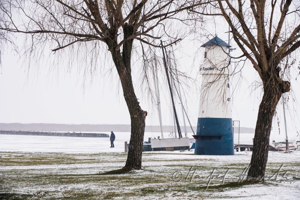 Leuchtturm im Hafen und Eisläufer auf dem See