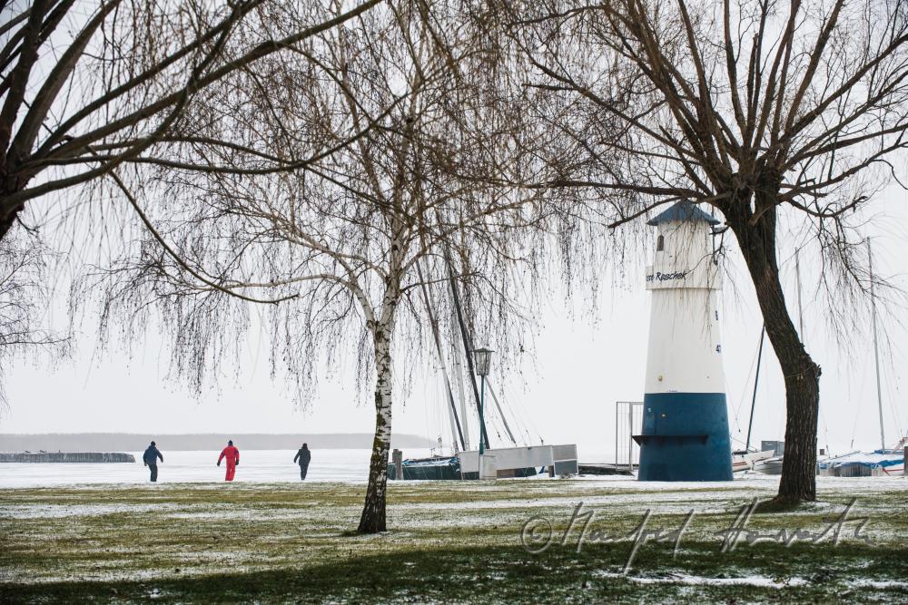 Leuchtturm im Hafen und Eisläufer auf dem See