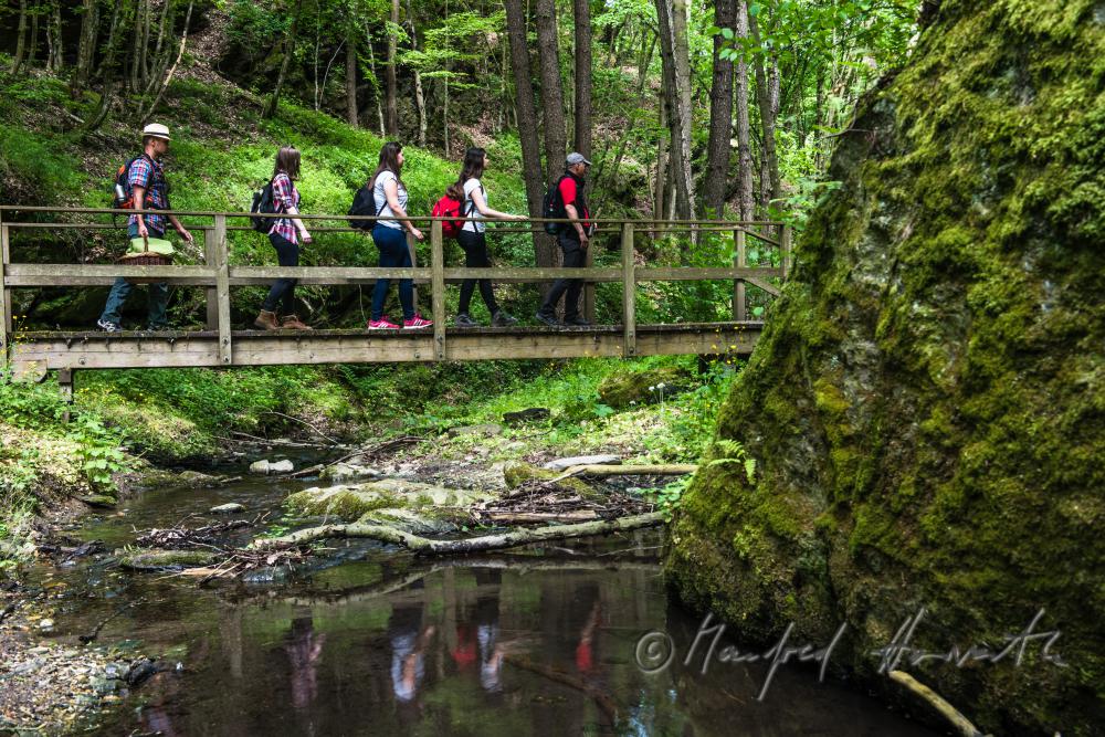 Wanderer überqueren eine Holzbrücke über den Kajabach